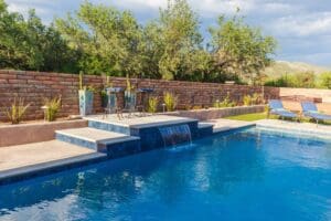 Backyard pool with waterfall and chairs.